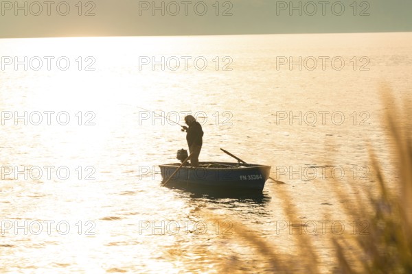 An angler fishing from a boat in the golden light of sunset, Überlingen, Lake Constance, Germany