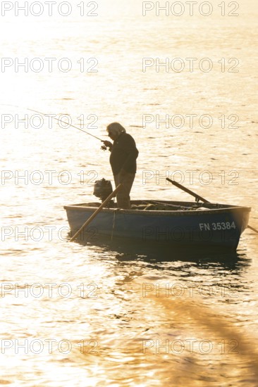 Single fisherman in a small boat fishing in the setting sun, Überlingen, Lake Constance, Germany