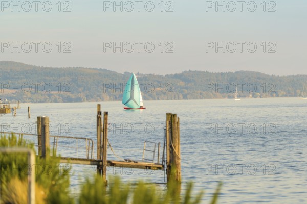 A sailboat sails across a calm lake under a blue sky, Überlingen, Lake Constance, Germany