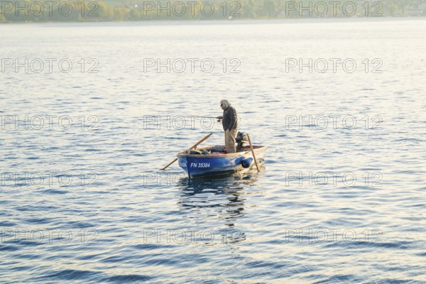 A man fishing alone on a small boat on a quiet lake, Überlingen, Lake Constance, Germany