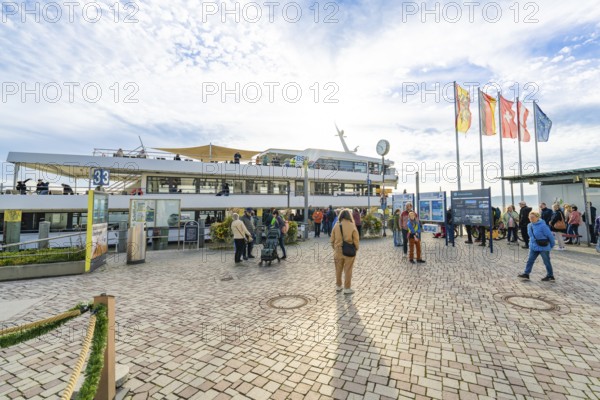People at the harbor in sunny weather and blue sky, surrounded by flags and ships, Überlingen, Lake Constance, Germany