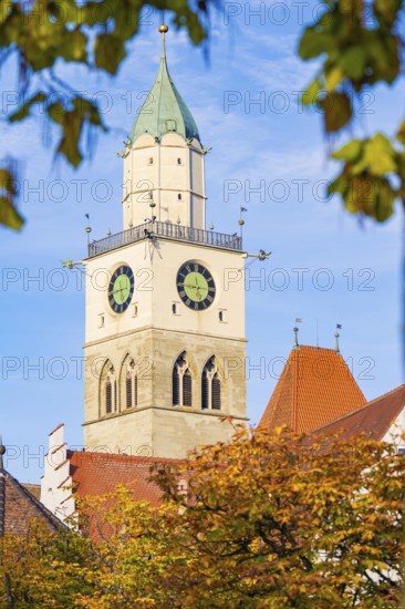 A church tower with clocks rises into the blue autumn sky, surrounded by autumn leaves, Überlingen, Lake Constance, Germany