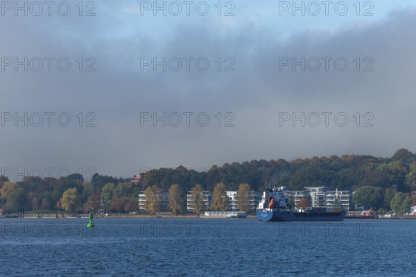 Kiel Fjord, Holtenau district, Kiel, modern apartments on the river bank, cargo ship, hillside, forest, Baltic Sea, Schleswig-Holstein, Germany