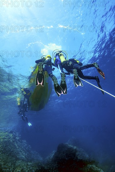 Underwater photo Group of scuba divers climb up to the sea surface at the end of dive on anchor rope from small boat dive ship, Mediterranean Sea, Majorca, Spain