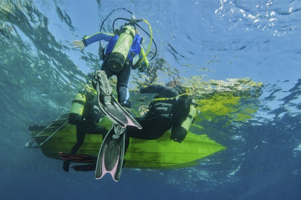 Underwater photo Group of scuba divers climb up to the sea surface at the end of dive on anchor rope from small boat dive ship, Mediterranean Sea, Majorca, Spain