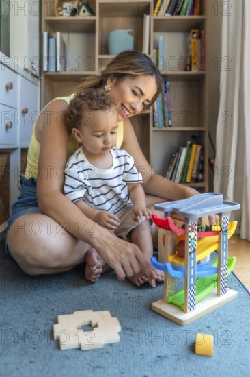 Smiling mother and son playing with a toy car and garage, enjoying quality time together in their living room