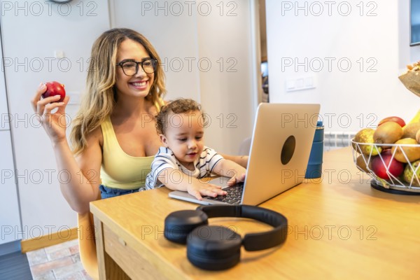 Happy mother working from home, eating healthy and taking care of her baby, while her son is playing with the laptop