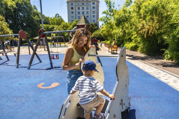 Mother helping her son enjoy a sunny day at the playground, happily playing together on a rocking horse amidst laughter and joy