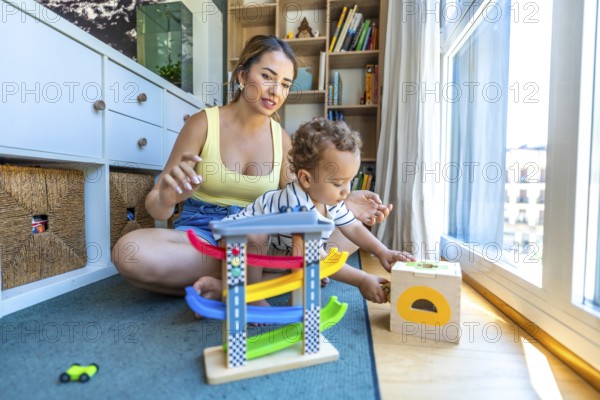 Young mother watching her baby son playing with a toy car garage and a shape sorter on the floor at home