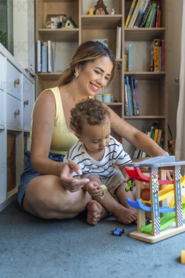 Happy mother and son playing with toy cars and garage, sitting on the floor in the playroom, having fun together