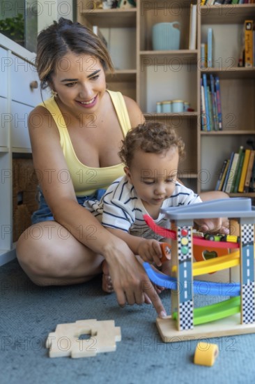 Mother and baby son sitting on the floor, joyfully playing together with a colorful toy car and ramp, fostering fun and bonding moments