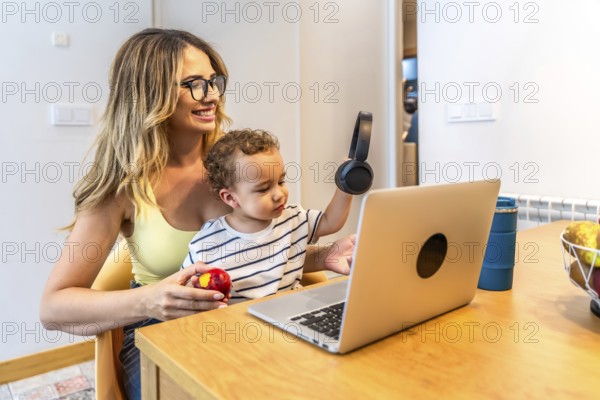 Mother and son sharing a moment of connection while using a laptop and headphones in their modern kitchen