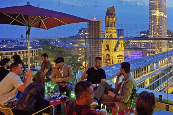 People on an outdoor terrace in the evening with a view of the illuminated Kaiser Wilhelm Memorial Church, Charlottenburg, Berlin, Germany