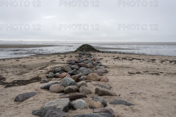 A stone groyne made of large granite blocks stretches from the sandy beach on the island of Föhr far into the mudflats, Schleswig-Holstein, Germany