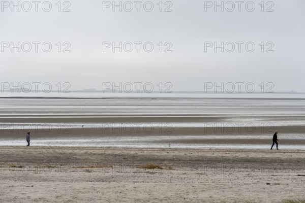 Two people walking on the wide beach of the island of Föhr, Schleswig-Holstein, Germany, at low tide