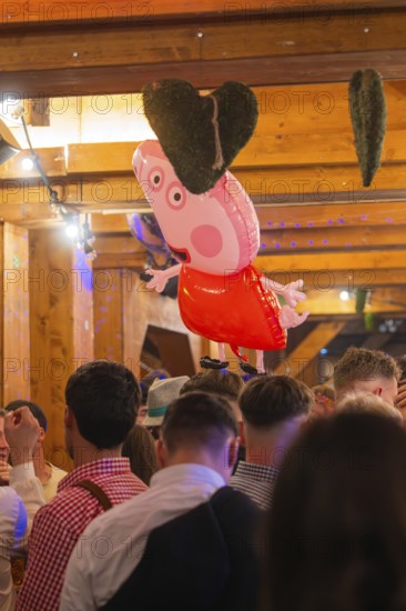 A pink heart-shaped balloon floats above a crowd in a traditional wooden house, Cannstatter Wasen folk festival, Sonja Merz marquee, Stuttgart, Germany