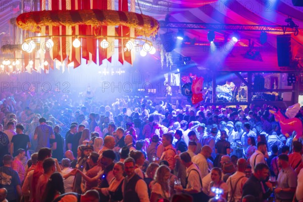 A lively party in a festive beer tent with stage and illuminated atmosphere at night, Volksfest Cannstatter Wasen, Sonja Merz Festzelt, Stuttgart, Germany