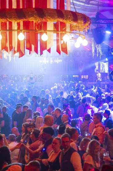 Large crowd celebrating in a beer tent under colourful lights and enjoying the music, Volksfest Cannstatter Wasen, Sonja Merz Festzelt, Stuttgart, Germany