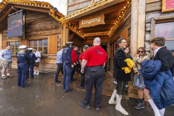 People in traditional Bavarian dress and police gather in front of a festively illuminated wooden entrance, Cannstatter Wasen folk festival, Sonja Merz marquee, Stuttgart, Germany