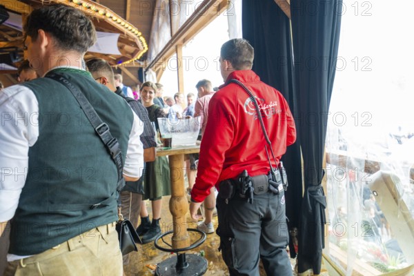 People in traditional traditional costume and security service stand in a crowded interior with wooden elements, Cannstatter Wasen folk festival, Sonja Merz Festzelt, Stuttgart, Germany