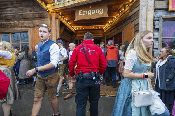 Visitors in traditional traditional costume leaving a wooden entrance at the Oktoberfest while security is present, Volksfest Cannstatter Wasen, Sonja Merz Festzelt, Stuttgart, Germany