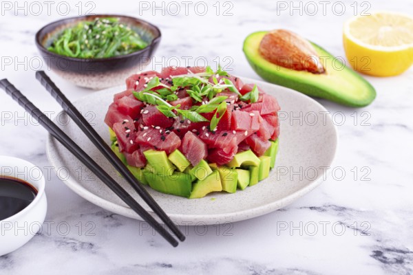 Fresh tuna tartare with avocado served on a marble table with soy sauce and seaweed salad