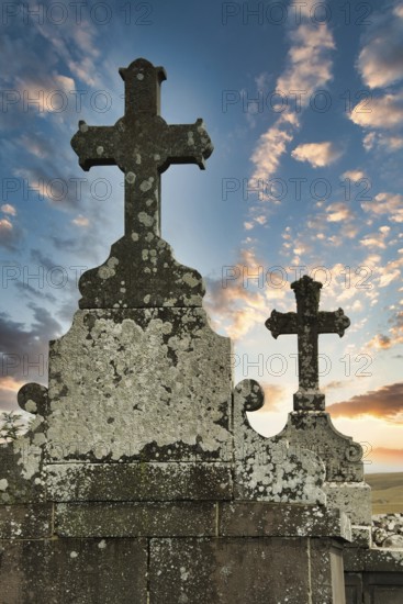 Two weathered crosses stand tall against a colorful sunset sky, showcasing the beauty of an ancient cemetery. Cantal. Auvergne Rhone Alpes. France