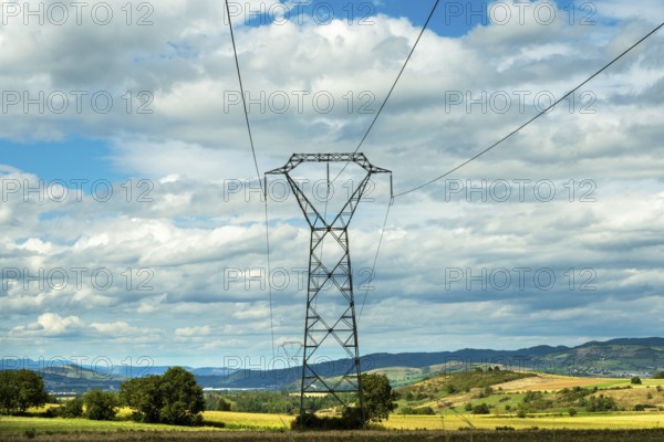 High voltage power lines against a bright blue sky with scattered clouds, Puy de Dome, Auvergne Rhone Alpes, France