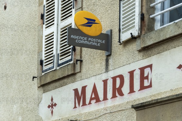 A postal agency sign is seen at the town hall in Auvergne Rhone Alpes, France. This setting reflects community services and local governance. The architecture features traditional shuttered windows