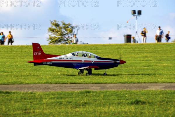 An RC model of a Pilatus PC-21 with advertising for the Swiss watch brand Breitling during a flight demonstration as part of an air show at the Rossfeld in Metzingen-Glems, Baden-Württemberg, Germany, for editorial use only