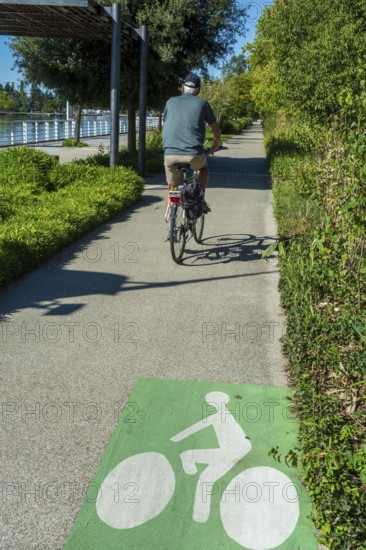 A person rides a bicycle on a smooth pathway lined with trees and shrubs. Vichy. Allier. Auvergne Rhone Alpes. France