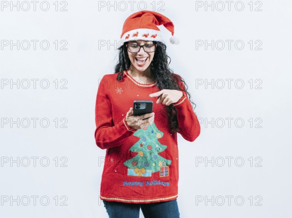 Happy girl in Christmas sweater looking pointing phone screen, isolated
