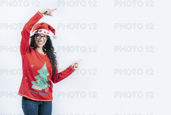 Smiling girl in Christmas sweater pointing to the side, isolated. Happy young woman in Christmas sweater recommending and pointing aside