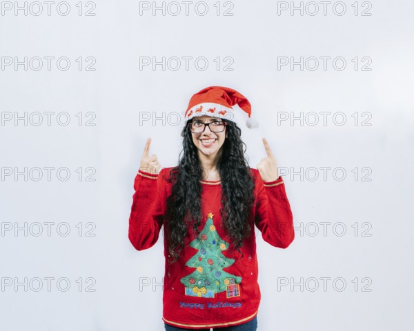 Smiling girl in Christmas hat pointing up isolated. Beautiful girl in Christmas sweater showing and pointing up