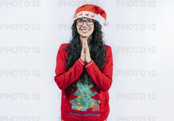 Supplicant girl in Christmas sweater making a wish, isolated. Young woman in a Christmas hat with palms together making a wish