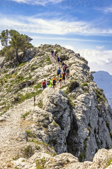 Group of people mountain hiking on a path by a steep rock in a mountainous landscape a sunny summer day, Mallorca, Spain