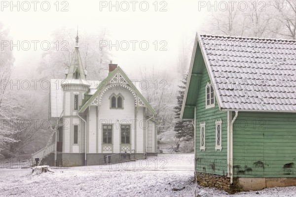 Old idyllic white wooden house with carpentry and a green garden shed on a cold winter day with snow and frost, Falköping, Sweden