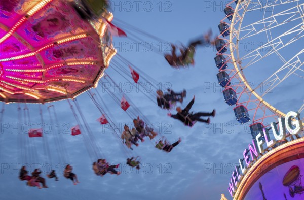 An illuminated chain carousel turns at night at a funfair, with floating people and colourful lights, Bad Cannstatt, Stuttgart, Baden-Württemberg, Germany