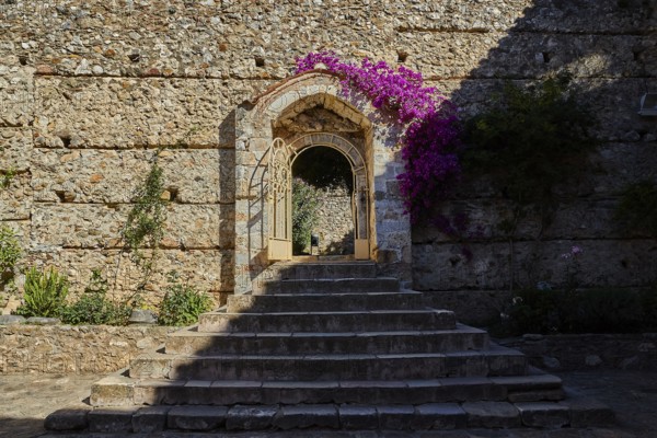 Metropolis, Metropolitan Church of Agios Dimitrios Mystras, A flower-covered stone gate in an ancient wall casts sharp shadows, Mystras, Mistra, UNESCO World Heritage Site, Medieval Byzantine ruined city, north-west of Sparta, Taygetos foothills, Peloponnese, peninsula, Greece
