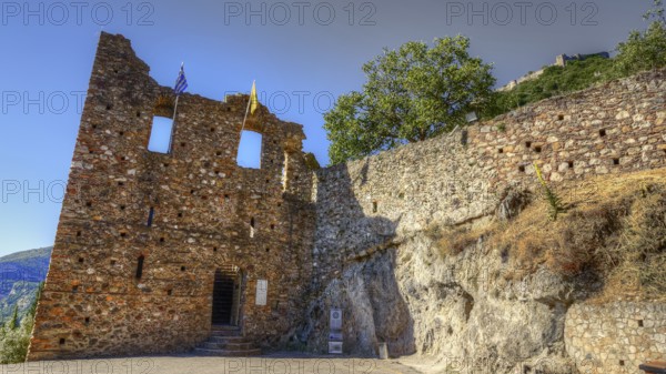 Lower main entrance, Historic ruins with flags in front of stony terrain under blue sky, Mystras, Mistra, UNESCO World Heritage Site, Medieval Byzantine ruined city, northwest of Sparta, foothills of the Taygetos Mountains, Peloponnese, peninsula, Greece