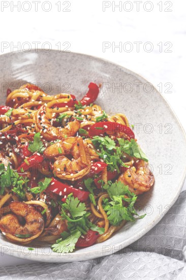 Udon noodles, shrimp with vegetables and fresh herbs, in a bowl with chopsticks, light background, homemade, no people