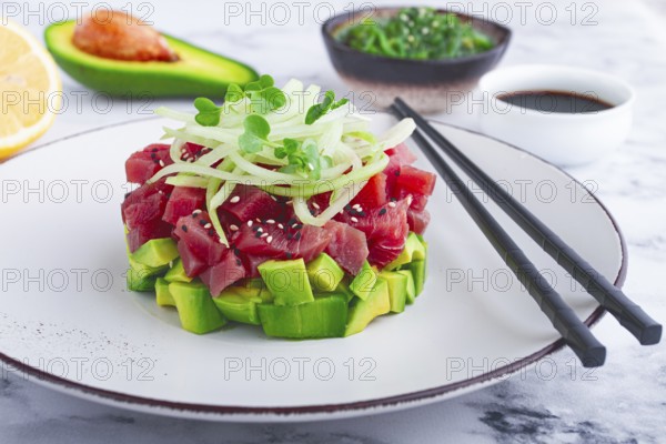 Fresh tuna tartare with avocado served on a marble table with soy sauce and seaweed salad