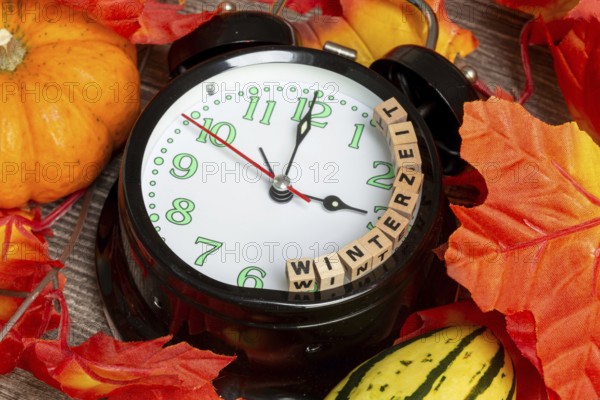 Winter time changeover: close-up of an alarm clock, autumnal decoration and letter cubes displaying the word WINTER TIME