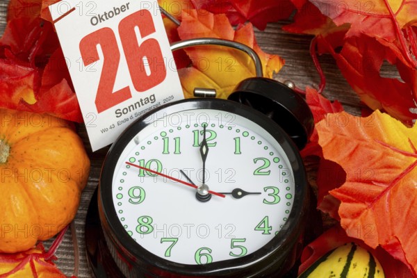 Time changeover to winter time 2025: Close-up of an alarm clock, autumnal decoration and a page from a tear-off calendar showing the date 26 October