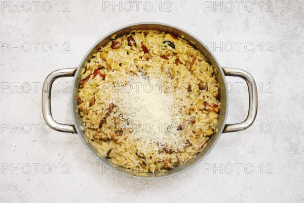 A delicious risoni dish with porcini mushrooms is presented in a pan. This comforting meal is topped with freshly grated parmesan cheese, showcasing a blend of flavors. Perfect for dinner enjoyment