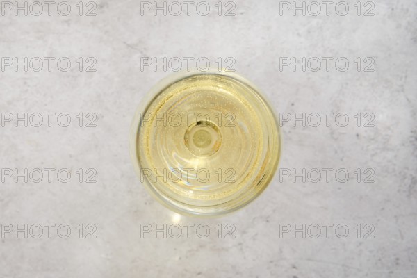 Close-up overhead view of a glass filled with white wine on a light textured surface