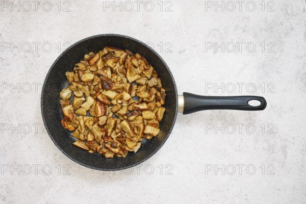 Diced porcini mushrooms are frying in a black pan, creating a savory meal. The cooking process showcases golden-brown pieces and a delicious aroma filling the kitchen