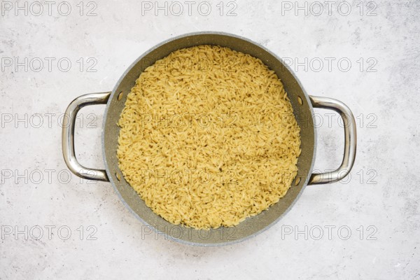 A pot filled with perfectly cooked risoni pasta on a neutral surface. This dish showcases a rich golden color, hinting at flavorful ingredients and a warm home cooking atmosphere