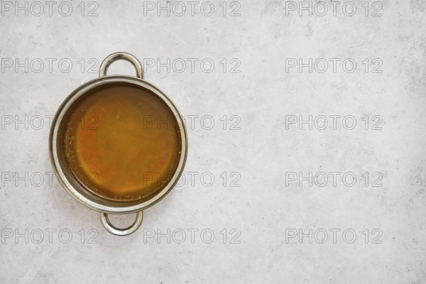 A silver pot filled with rich, golden mushroom broth on a smooth light gray surface. The broth appears warm and inviting, perfect for soups or hearty dishes