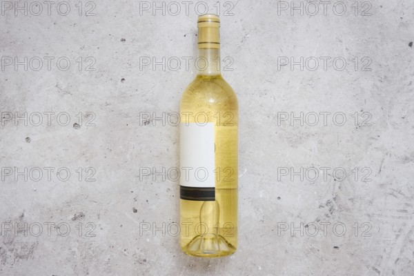 A white wine bottle with a blank label on a light grey textured surface. The setting suggests a calm moment for wine tasting or a casual gathering with friends